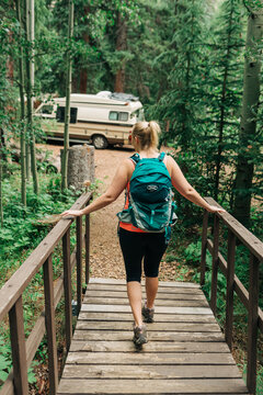 Woman hiking across bridge toward camper in forest near Bailey,