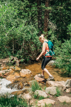 Woman hiking and crossing rocky creek on Deer Creek Trail, Color