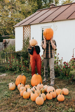 Father and daughter hold pumpkins in front of faces in garden