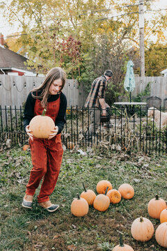 Father and daughter work together harvesting pumpkins in yard