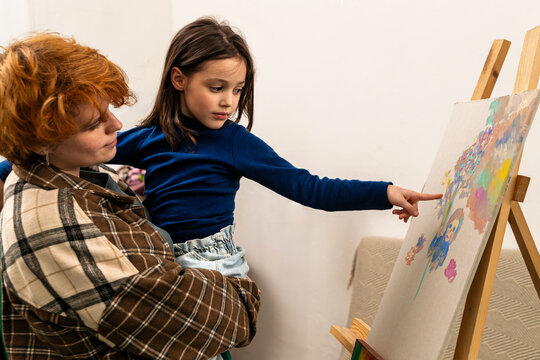 mother, an artist, shows her daughter her drawing on the easel.