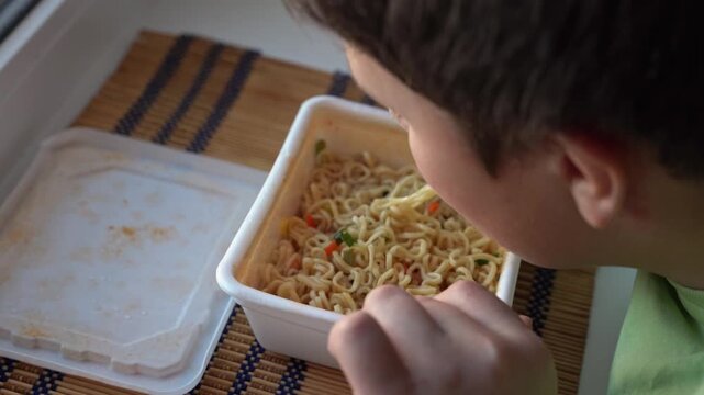 Boy enjoys eating noodles from a container on a table at home in the afternoon
