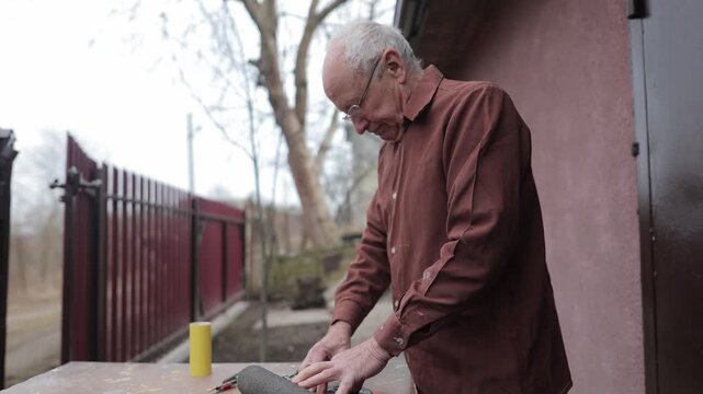 Elderly man concentrating while sharpening tools outdoors