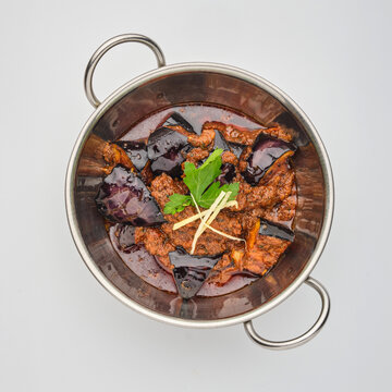Delicious dish served in a metal bowl with eggplant, meat, and spices placed on a white surface