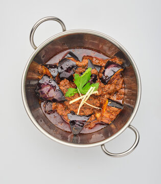 Spicy eggplant curry cooked in a stainless steel pot with herbs and spices on a plain background