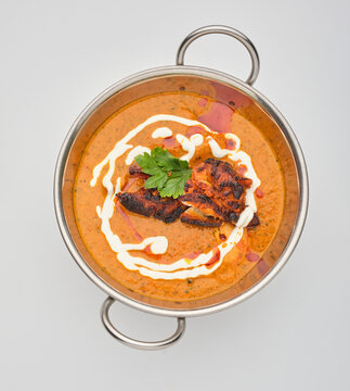 Dish of cooked chicken in sauce served in a bowl with garnishes and swirl of cream seen from above in a modern setting