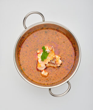 Hot soup with a small piece of meat and a green leaf placed on top served in a bowl on a plain surface