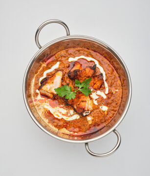 Dish served in a metal bowl with sauce, chicken pieces, and herbs on a plain background in a kitchen setting