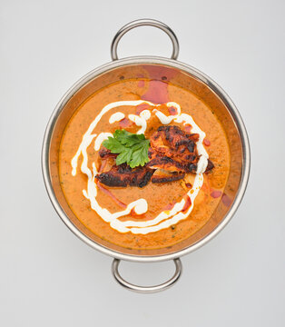 Butter chicken served in a round metal dish with sauce and toppings on a plain background