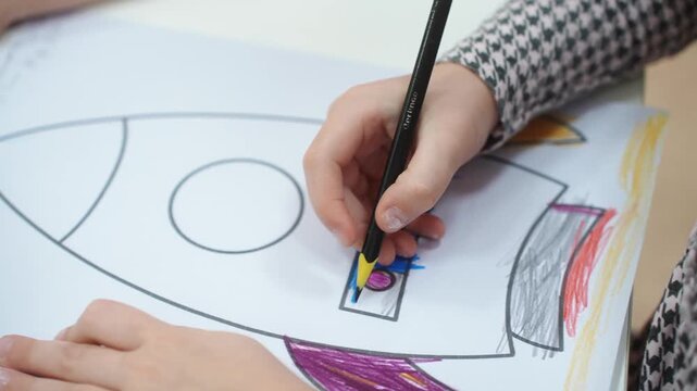 A girl draws a rocket with a pencil in kindergarten. Close-up. High quality video