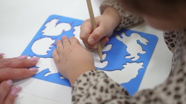 A girl on a stencil circles animals with a pencil. Kindergarten classes. Close-up. High quality video