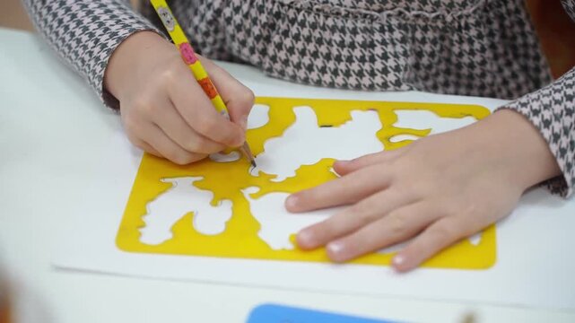 A girl on a stencil circles animals with a pencil. Kindergarten classes. Close-up. High quality video