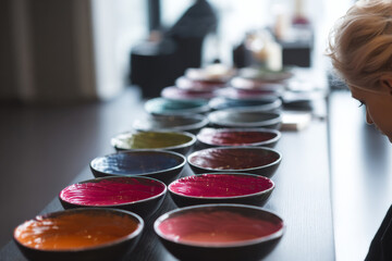 colorist preparing multiple bowls of different hair dye shades, client in background, minimalist beauty studio, professional lighting setup