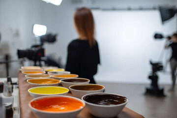 colorist preparing multiple bowls of different hair dye shades, client in background, minimalist beauty studio, professional lighting setup