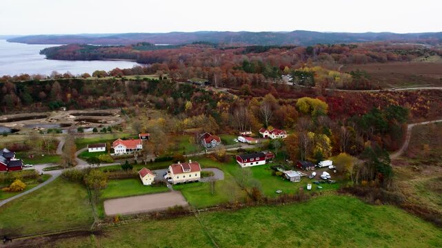 Aerial drone view of rural farms and villas at Fjaras Bracka in Sweden surrounded by autumn forest, open fields, countryside roads and natural landscape near lake