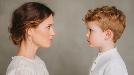 Intimate side profile studio portrait of a mother and her young son capturing a moment of deep connection and shared curiosity against a clean neutral background