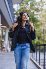 Fototapeta premium Young woman walking listening to music smiling outdoors