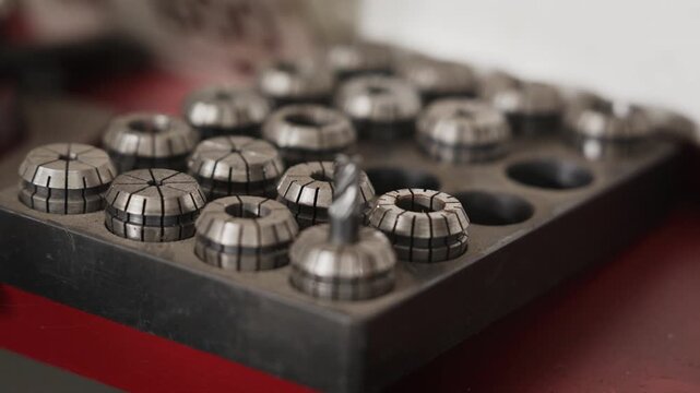Close-up of a workshop tray filled with steel CNC machining collets, focusing on an end mill cutting tool