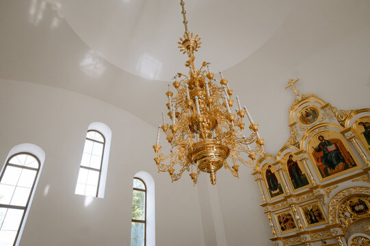 Ornate golden chandelier and iconostasis in white orthodox church interior