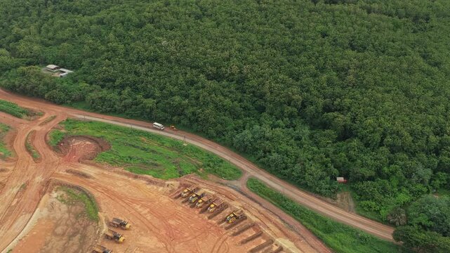Aerial footage showing a large construction site with heavy machinery encroaching upon a lush green forest, highlighting deforestation