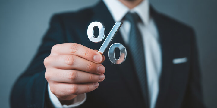 A businessman presenting a metallic percent sign symbolizing finance and economic concepts.