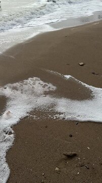 Sea waves rolling on sandy beach with birds flying under cloudy sky, vertical video