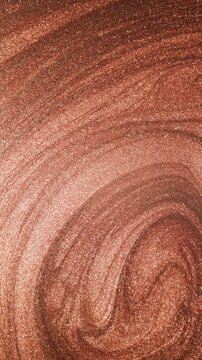 Mesmerizing vertical video of rose gold paint with sandy texture rotating and swirling slowly into elegant curves and shimmering with radiant glitter particles on abstract background