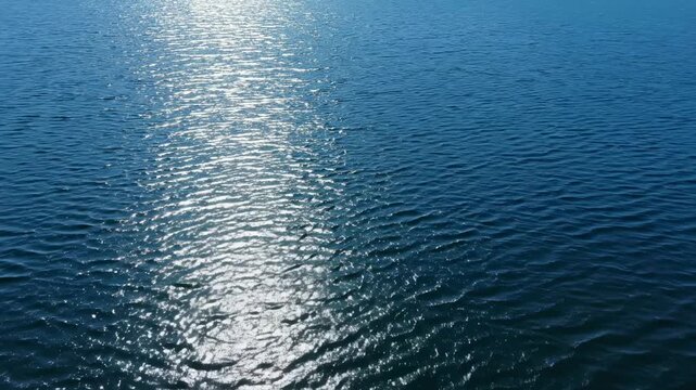 Sunlight reflecting on calm water surface, creating shimmering patterns and ripples, showcasing the tranquil beauty of a serene lake or ocean environment