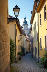 Obraz premium Narrow cobbled street in old European town center. Yellow buildings line historic path. Traditional lamp post on wall overlooks quaint walkway toward distant tower.