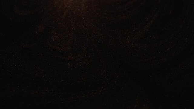 Dynamic close-up of dark rose gold paint swirling and spreading due to mixing with a wooden stick creating a prominent circular wave shape and displaying glittering particles on black background