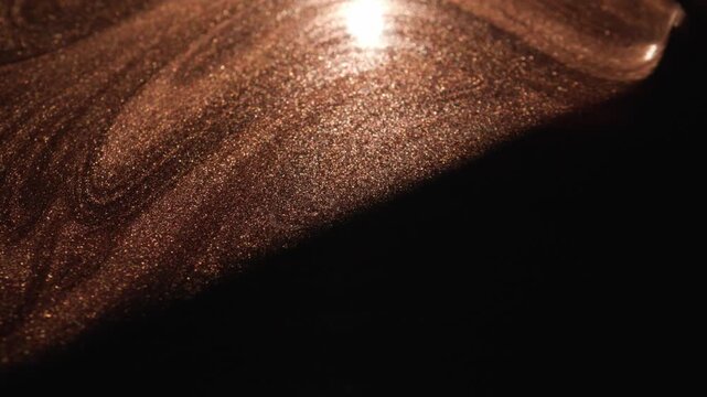 Mesmerizing close-up of rose gold paint with radiant glitter particles obscured by a moving shadow that sweeps across the surface revealing the textured shimmer on dark background