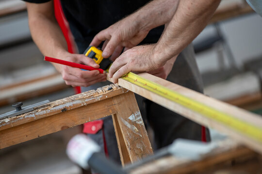 Menuisier effectuant une mesure avec un m&egrave;tre sur une planche de bois sur des tr&eacute;teau &agrave; l'int&eacute;rieur d'un b&acirc;timent. Menuisier exp&eacute;riment&eacute;, habile et comp&eacute;tent, prenant des mesures pour cr&eacute;er un meuble