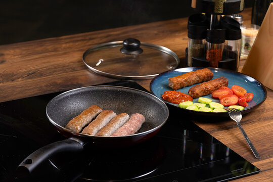 Traditional Balkan grilled minced meat dishes, kebapcheta and meatballs, being cooked in a frying pan in a home kitchen
