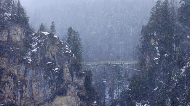 Cinematic winter video of the famous Marienbr&uuml;cke (Mary's Bridge) spanning across a deep gorge near Neuschwanstein Castle during a heavy snowstorm, Bavaria, Germany.