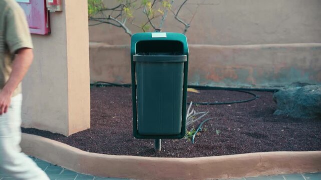 ideo of a classic outdoor trash bin with centered composition as someone throws away waste, symbol of cleanliness, disposal, responsibility and everyday urban routine