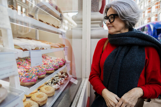 Mature woman with gray hair admiring donuts at bakery window