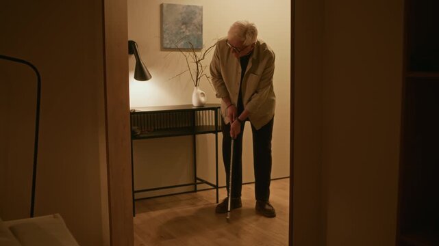 Full shot of senior Caucasian man hitting golf ball with putter while standing in modern living room, enjoying hobby indoors