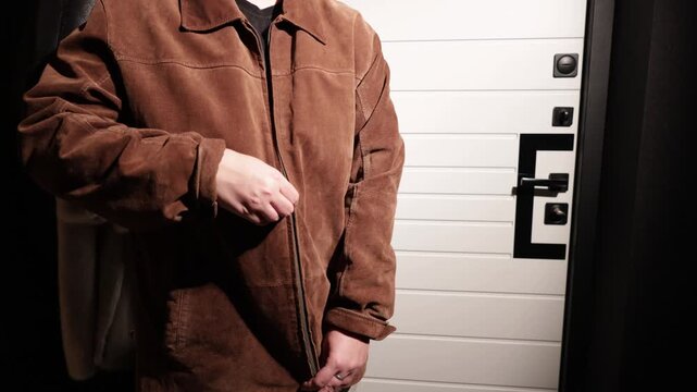 Person zipping up a brown suede jacket in front of a modern garage door