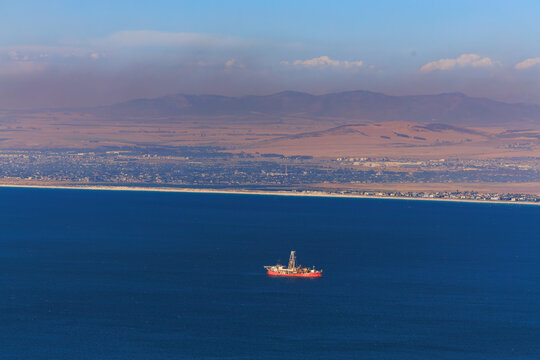 Aerial view of a solitary oil rig stands out against the deep blue ocean, contrasted by the distant, hazy mountain range, Cape Town, Western Cape, South Africa.