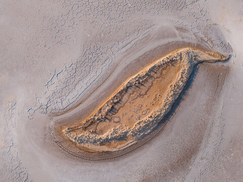 Aerial view of a stark, cracked earth landscape cradling a small, sandy island with deep shadows, Lake Campion Nature Reserve, Western Australia, Australia.