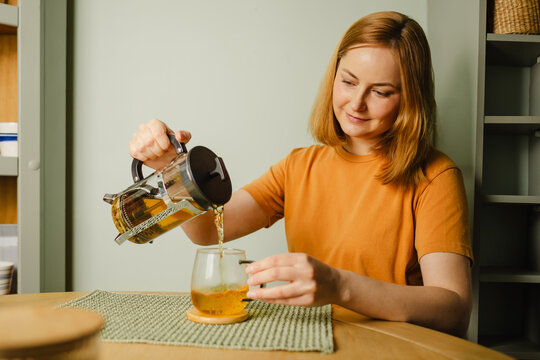 Woman pouring organic herbal tea from french press in kitchen