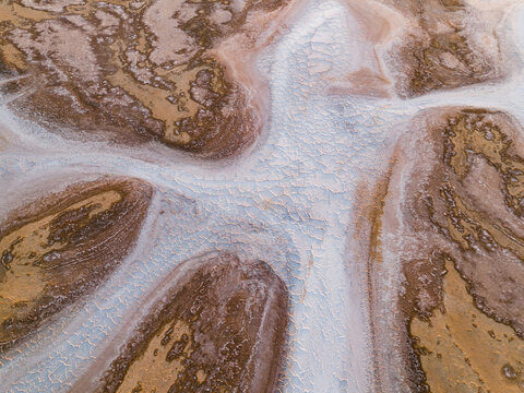 Aerial view of parched earth kissed by a silver vein, where ochre textures meet the stark white of cracked salt flats, Lake Campion Nature Reserve, Western Australia, Australia.