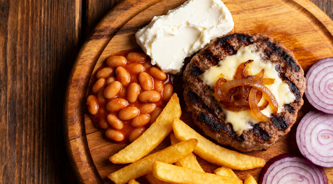 Delicious grilled pljeskavica with kajmak, prebranac, fries and fresh red onion on wooden board.