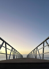 Fototapeta premium The pier extending out over the water into a vast, pastel-colored sky at sunset.Powerful background for a reel about journey, reflection, or the beauty of nature.