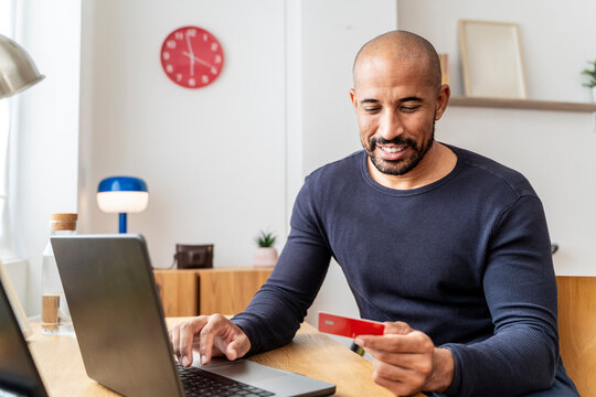 Smiling man shopping online with credit card at home workspace