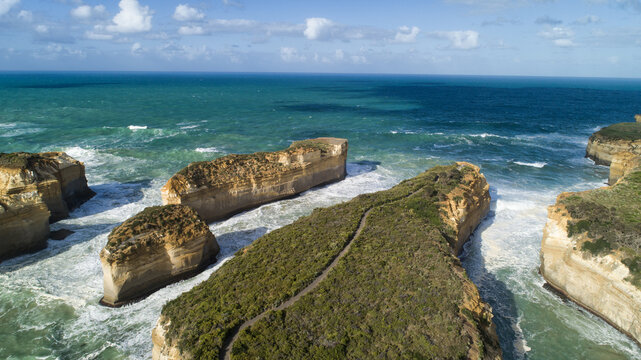 Aerial view of imposing limestone stacks rise majestically from the turquoise ocean, a rugged coastline carved by time and tide, Port Campbell, Victoria, Australia.