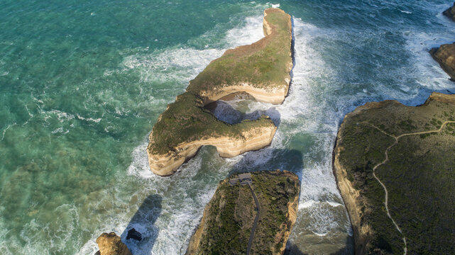 Aerial view of craggy cliffs meet the turquoise sea along the Great Ocean Road, where waves crash against the weathered rock formations, Port Campbell, Victoria, Australia.