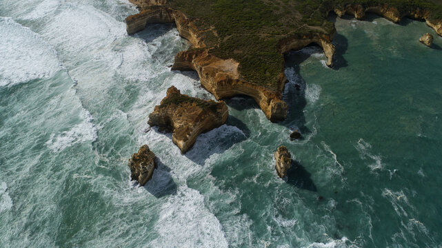 Aerial view of the rugged coastline where the turquoise waters clash against the weathered cliffs and scattered rock formations, Port Campbell, Victoria, Australia.