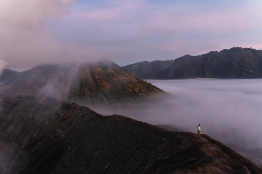 Person standing on ridge at sunrise with fog over Mount Bromo volcano