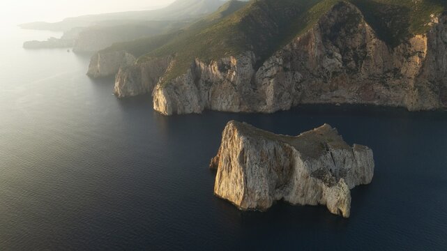 Aerial view of craggy cliffs meet the deep blue sea, a stark contrast of textures and tones under the soft, diffused sunlight, Masua, Sardegna, Italy.